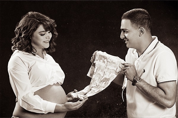 عکس سیاه وسفید بارداری زوج در حال نگاه کردن به لباس نوزاد